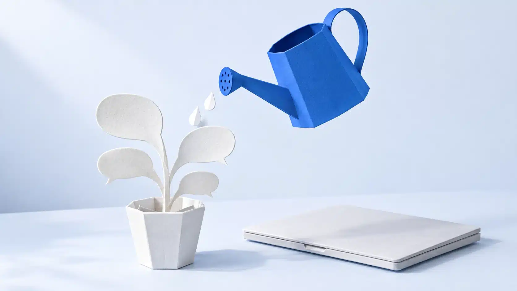 Eine blaue Gießkanne gießt auf eine weiße Papierpflanze mit Sprechblasen als Blättern; daneben liegt ein geschlossener Papier-Laptop.