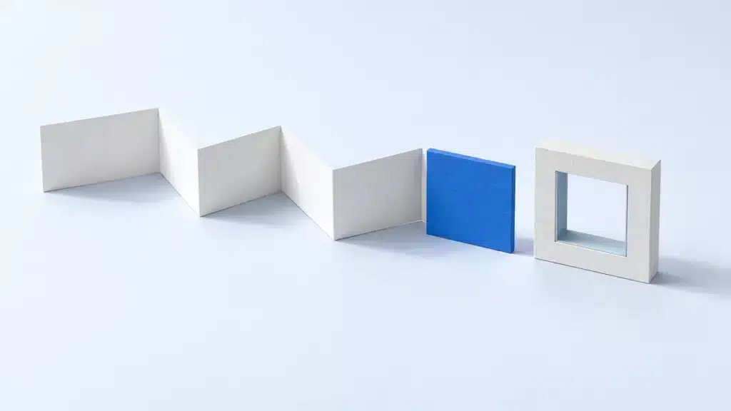 Eine gefaltete weiße Papierbahn endet an einer blauen quadratischen Platte. Daneben steht ein weißer Kartonrahmen mit quadratischer Öffnung. (KI-generiert)